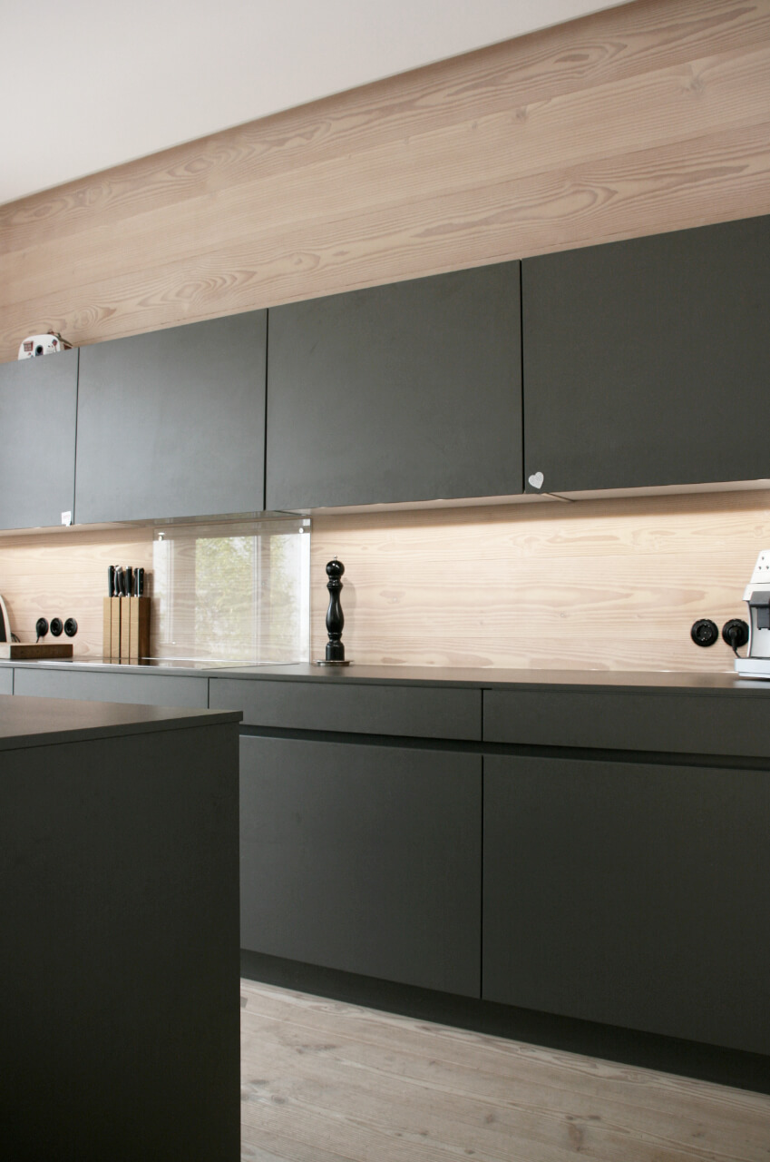 Schwarze Wohnküche mit Wandverkleidung aus Holz sowie Dielenboden