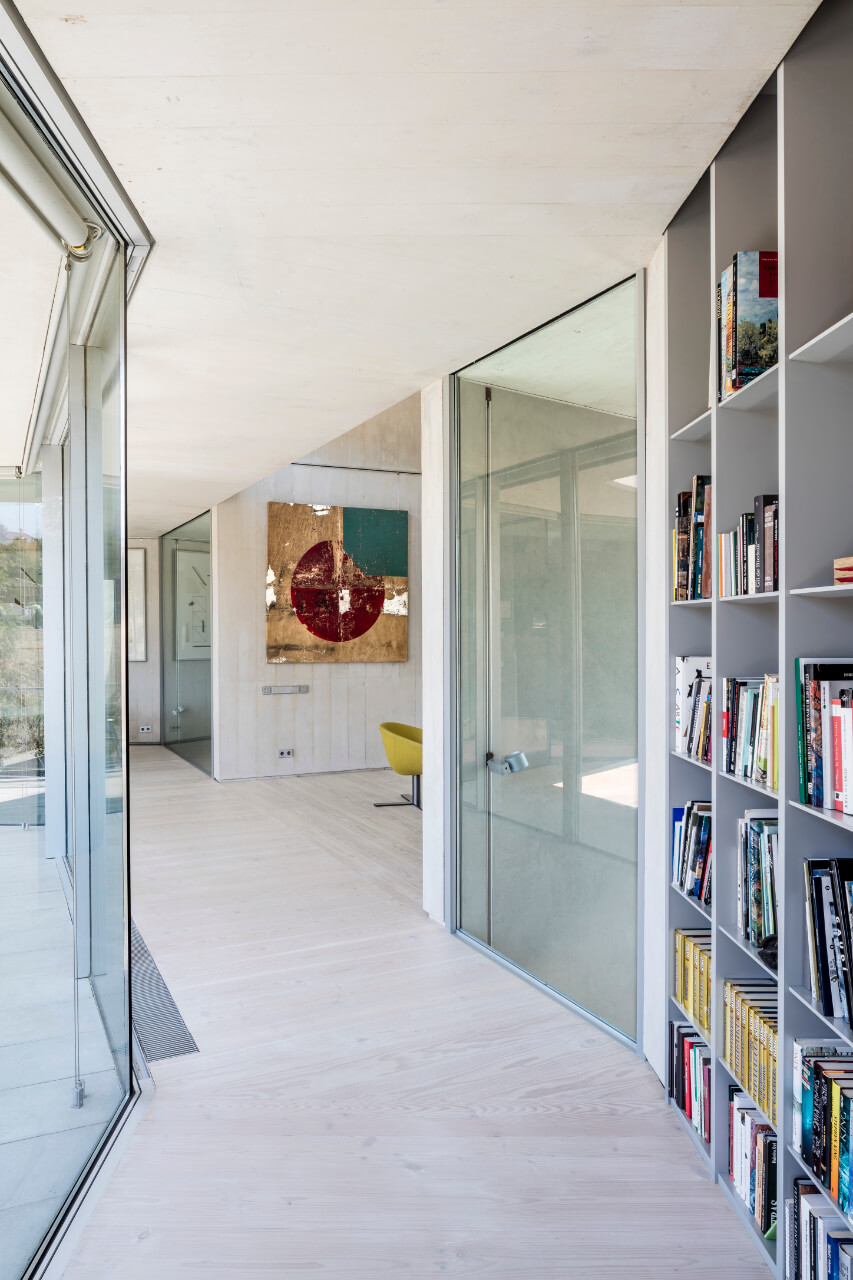 Um die Ecke führender heller Gang mit hellem Dielenboden, Fensterseite und Bücherregal