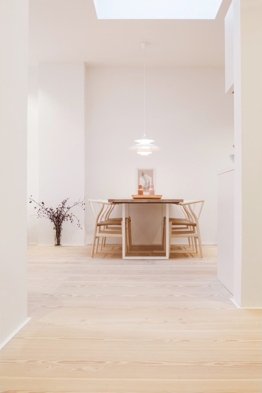 Offenes Esszimmer mit weißen Wänden, hellem Dielenboden und hellem Esstisch mit Stühlen